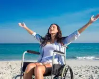 10 Wheelchair-Accessible Destinations You Won't Want to Miss Disabled woman with arms outstretched at the beach on a sunny day